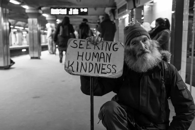 Man with Sign Saying "Seeking Human Kindness" by Matt Collmer for Unsplash.Survival Prepping 101 Series Part 8: FinancesSurvivalPrepperSupply.com